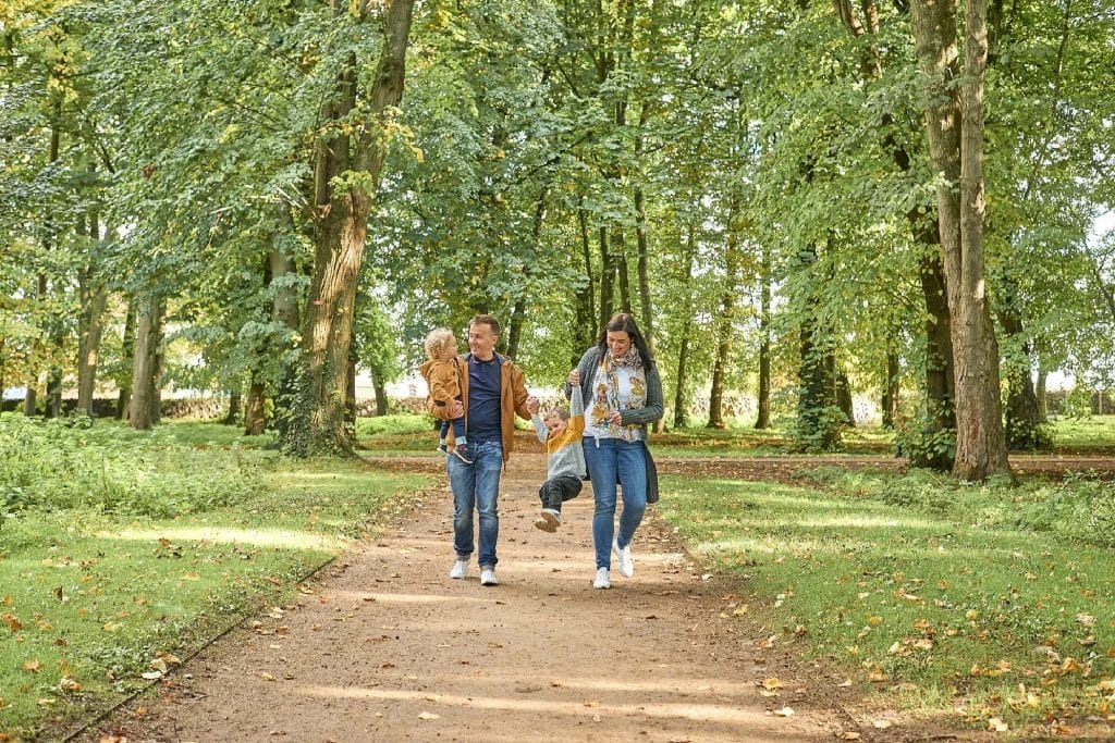 Family Photographer Two individuals walking together on a tree-lined path in a park.