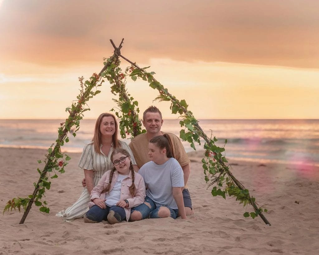 Family Photographer A Ballymoney family poses in front of a teepee on the beach.